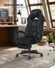 A black gaming chair with yellow accents is shown in a home office setting with a desk, computer, and window in the background. Produktbild-Vorschau