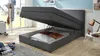 A dark gray storage bed with its lid open, revealing pillows and blankets inside. The room has a blue wall and a window in the background. Produktbild-Vorschau