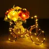 A decorative metal bicycle holding a vase of flowers, illuminated by warm white string lights. Produktbild-Vorschau