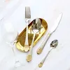 A collection of silverware, including a fork, knife, and spoons, arranged on a marble-like surface next to a wine glass and a gold tray. Produktbild-Vorschau