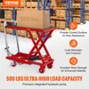 A red hydraulic scissor lift table with a box on top, in a warehouse setting. Voir les images du produit