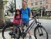 A man and a child stand next to an electric bicycle on a city street. Anteprima dell’immagine prodotto