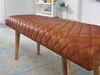 A close-up shot of a brown leather bench with a diamond-stitched pattern, resting on wooden legs. Produktbild-Vorschau