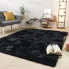 A black shaggy rug is laid out on a light wooden floor in a modern living room setting, with a grey armchair, side tables, and a floor lamp visible. Produktbild-Vorschau