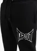 A close-up of black sweatpants with a white Tapout logo. Produktbild-Vorschau