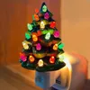 A ceramic Christmas tree night light plugged into a wall socket. Náhľad obrázku produktu