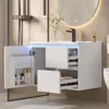 A modern white bathroom vanity with an open door revealing storage and drawers, featuring a black faucet and a round illuminated mirror above. Náhľad obrázku produktu