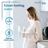 A woman is pouring water from a pitcher into a glass in a kitchen setting. Anteprima dell’immagine prodotto