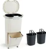 A beige multi-compartment trash can with a lid and a pull-out drawer, shown next to two black bins with handles. Anteprima dell’immagine prodotto