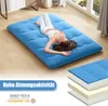 A woman is lying on a blue floor mattress in a room with wooden floors and large windows. Produktbild-Vorschau