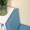 A close-up view of a blue upholstered bench next to a white surface, possibly a shelf or table, with a glass vase containing green leaves on the white surface. Produktbild-Vorschau