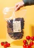 A hand holds a large bag of dried tomatoes, with fresh tomatoes in the foreground. Produktbild-Vorschau