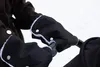 A person's hands wearing black stroller hand warmers with white trim are gripping the handle of a stroller. Náhľad obrázku produktu