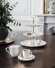 A table setting with a tiered cake stand filled with sweets and a coffee cup and creamer. Produktbild-Vorschau