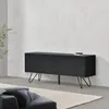 A dark gray sideboard with metal legs is placed against a textured white wall in a modern living room setting. A rug is on the floor in front of the sideboard, and a portion of a gray sofa is visible in the foreground. Podgląd zdjęcia produktu