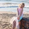 Mädchen sitzt am Strand in Meerjungfrauenverkleidung auf einer Schatztruhe, bunte Perlenketten hängen heraus. Produktbild-Vorschau