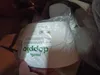 A hand holding a white plastic planter pot, which is partially wrapped in plastic packaging. The pot has green text on it. Náhled obrázku produktu