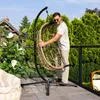 A man is standing on a balcony, holding a hanging chair. There are trees and a house in the background. Produktbild-Vorschau