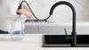 A person is filling a glass pitcher with water from a black kitchen faucet in a modern kitchen. Produktbild-Vorschau