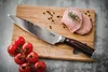 A chef's knife is placed on a wooden cutting board next to cherry tomatoes and slices of meat. Voir les images du produit