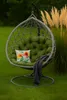 A hanging egg chair with a green cushion, a floral pillow, and a gray blanket, placed on a green lawn with tall, tan grasses in the background. Voir les images du produit