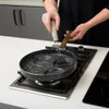 A person is using a brush to oil a non-stick pan with multiple circular indentations on a gas stove. Produktbild-Vorschau
