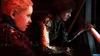Two characters are looking intently at something off-camera, with one character's arm extended towards a red light. Produktbild-Vorschau