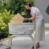 A woman is placing a mosquito net over a baby bassinet outdoors. Anteprima dell’immagine prodotto