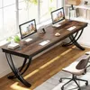 A long, dark wood desk with two computer monitors, office supplies, and a chair in a well-lit room with large windows. Podgląd zdjęcia produktu