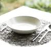 A placemat with a bowl and cutlery set on a white table. Voir les images du produit