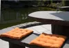 Two orange seat cushions are placed on a stone bench next to a pond. Produktbild-Vorschau