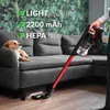 A person using a cordless vacuum cleaner in a living room with a dog on the couch. Voir les images du produit