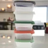 A stack of clear plastic food storage containers with colored lids in a kitchen setting. Produktbild-Vorschau