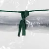 A close-up of a green ribbon tied around a clear plastic tube, which contains rolled-up material. Produktbild-Vorschau