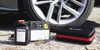 A tire repair kit and compressor are placed on the ground next to a car tire. Produktbild-Vorschau