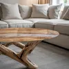 A close-up of a unique coffee table with a natural wood and resin top, placed in a living room setting with a sofa in the background. Podgląd zdjęcia produktu