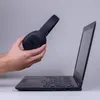 A person is holding a pair of black headphones over an open laptop. Produktbild-Vorschau