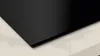 A close-up view of the corner of a black induction hob resting on a marble-patterned countertop. Voir les images du produit