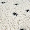 A close-up view of a fluffy, high-pile rug with a pattern of black dots on a beige background. Produktbild-Vorschau