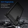 A black phone case with a brushed texture and carbon fiber accents is shown at an angle, with pieces of debris falling around it. Podgląd zdjęcia produktu