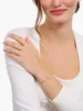 A woman wearing a white long-sleeved shirt and gold jewelry, including a ring and a bracelet. Anteprima dell’immagine prodotto