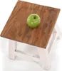 A green apple rests on a rustic wooden stool with white legs, set against a white background. Náhľad obrázku produktu