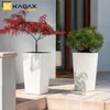 Two white planters with plants are placed on a patio next to a building entrance. Produktbild-Vorschau