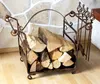A fireplace log rack filled with firewood, with a set of fireplace tools attached to the side, in front of a stone wall. Podgląd zdjęcia produktu