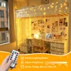 A hand holding a remote control in front of a bedroom decorated with string lights. Produktbild-Vorschau