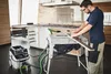 A man is using a table saw in a workshop setting, with a dust collector attached. Podgląd zdjęcia produktu