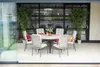 A round dining table with chairs on a patio, set with decorative pillows and vases. Produktbild-Vorschau