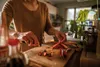 A person is chopping red chilies on a wooden cutting board in a kitchen. Podgląd zdjęcia produktu