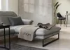 A modern living room with a grey sectional sofa and a throw blanket with the brand name 'JOOP!' on it. Produktbild-Vorschau