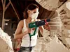 A woman is using a demolition hammer to break through a stone wall. Produktbild-Vorschau